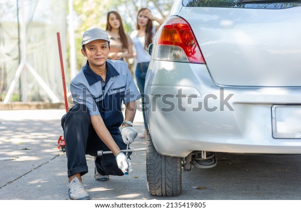 Expertise\
mechanic man  in uniform using force trying to unscrew the wheel\
bolts nuts and help a woman for changing car wheel on the highway,\
car service, repair, maintenance\
concept.