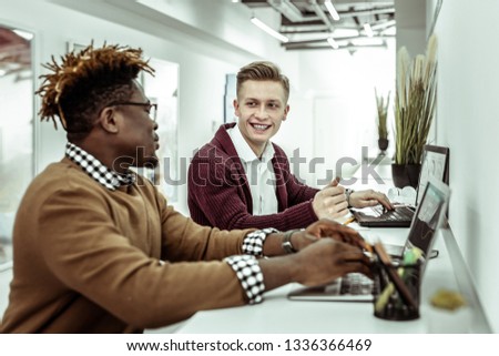Explaining idea. Smiling positive man in white shirt attentively listening to dark-skinned outgoing co-worker