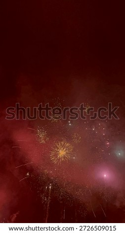 Exploding fireworks against a deep red misty night sky. Festive pyrotechnic display with sparks and smoke during celebration.