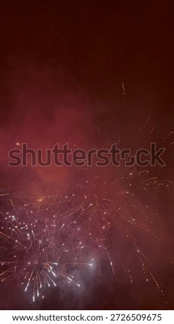 Exploding fireworks against a deep red misty night sky. Festive pyrotechnic display with sparks and smoke during celebration.
