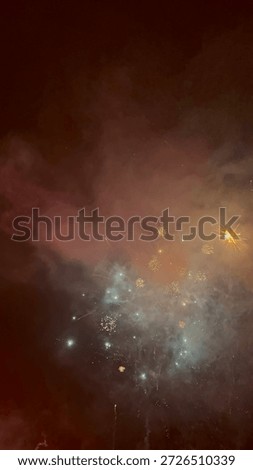 Exploding fireworks against a deep red misty night sky. Festive pyrotechnic display with sparks and smoke during celebration.