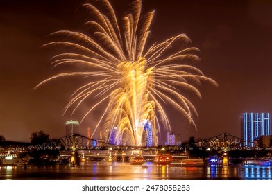 Exploding rockets in the night sky over the skyline of Frankfurt am Main with an iron footbridge and reflections on the River Main