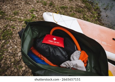 Explore musthave items for a fun day on the water, shown in this image with a waterproof bag of gear, clothing, and a first aid kit next to a paddleboard for a safe outdoor adventure