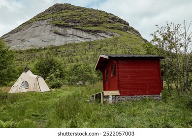 Explore the Serene Landscapes of Lofoten Islands With a Cozy Cabin and Tent Surrounded by Lush Greenery and Towering Hills - Powered by Shutterstock