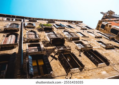 Explore the striking architecture of a Venetian building facade, featuring rustic brick walls and wooden shutters, highlighted by bright daylight from a low angle view. - Powered by Shutterstock