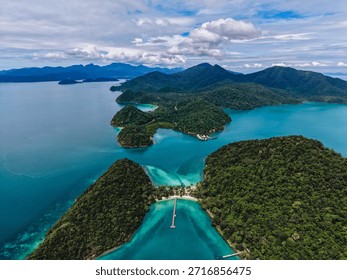 Explore the stunning aerial view of Ko Ngam beach in Koh Chang, Thailand, showcasing vibrant blue waters, green hills, and a peaceful landscape under a cloudy sky.