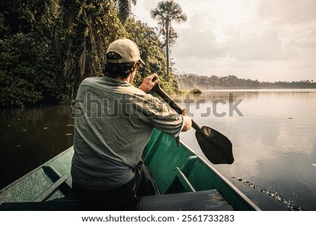 Explorer rowing on a canoe in the amazon rainforest during sunset