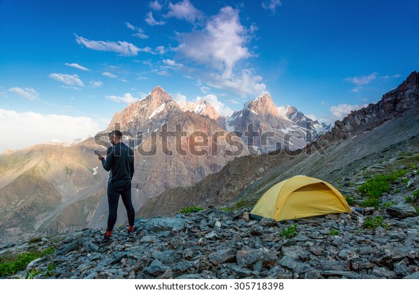 Explorer\
talking on satellite phone.\
Silhouette of man in wild mountain\
landscape walk along yellow camping tent holding radio transmitter\
connection with team blue sky sunny\
evening