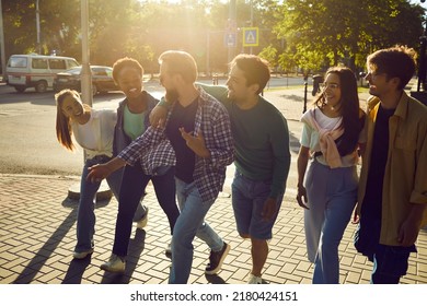 Exploring city together. Goup of cheerful friends walk streets of new city together during weekend vacation. Active millennial multiracial casual women and men laugh and talk while walking down street - Powered by Shutterstock