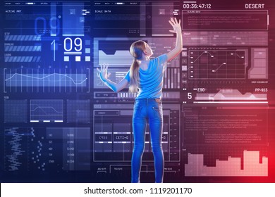 Exploring modern technologies. Progressive clever schoolgirl feeling curious and standing in front of a large transparent device while touching the screen of it and exploring modern technologies