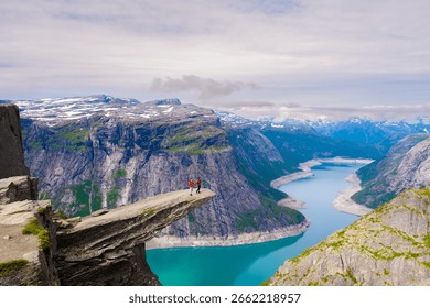 Exploring the stunning cliffs of Trolltunga, Norway, two hikers stand on the edge, overlooking the turquoise waters surrounded by majestic mountains.