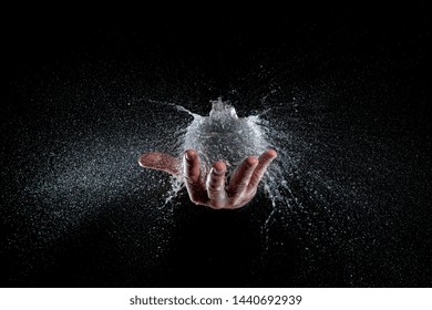 Explosion Of A Balloon Full Of Water Held On A Hand, Black Background Studio Shot. Hi Speed Photography