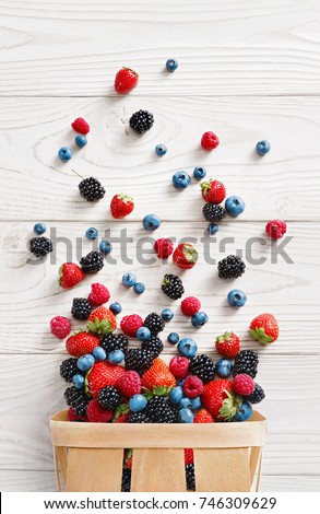 Explosion of different berries. Photo of strawberry, blueberry, blackberry, raspberry in basket on white wooden table. Top view. High resolution product. 