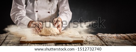Explosion of flour suspended in the air in a pizzeria kitchen as the chef prepares a portion of dough for the crust in a rustic panorama banner with copy space