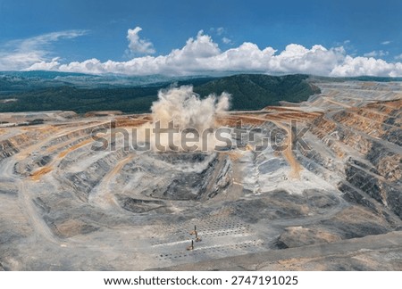 Explosive activity in vast open pit mine with dust cloud and terraced layers, Aerial panorama of industry landscape.