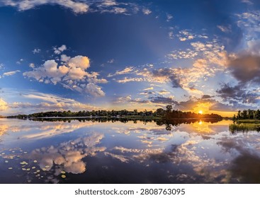 An explosive evening sunset with threads of neat cloud remnants arranged in dynamic, diagonal rows. Majestic orange patterns are symmetrically reflected in the calm river water. Tranquil spectacle.