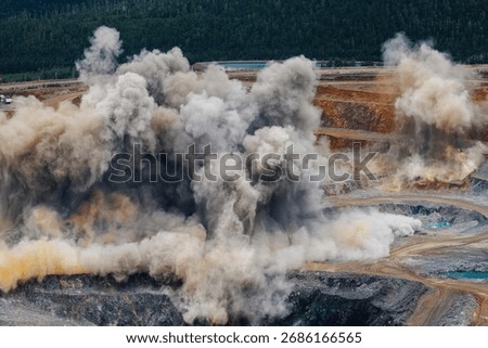 Explosive works on open pit gold mine industry with dust and puffs of smoke.