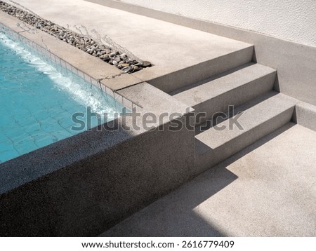 Exposed aggregate finish pool decks with steps with splashing water with no people. Abstract pool texture pattern, light blue background with grid tiles inside concrete building. Summer background.