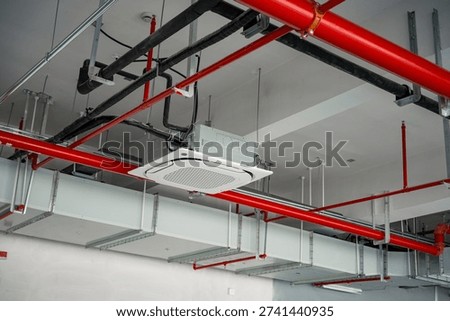 Exposed ceiling with red fire pipes black conduits and a suspended ceiling-mounted air conditioning unit