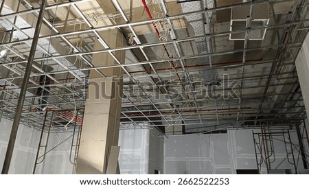 Exposed ceiling under construction showing metal framework, electrical wiring, and red sprinkler pipes. Interior renovation site in progress, industrial structure visible.