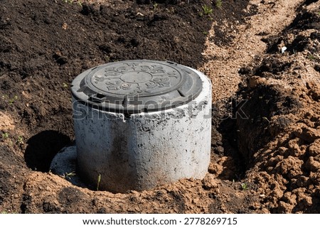 Exposed Concrete Access Ring In Soil, Urban Construction Site Showing Open Excavation, Worn Metal Cover, Compacted Earth, Heavy Equipment Tracks, Municipal Utility Upgrade, Inspector
