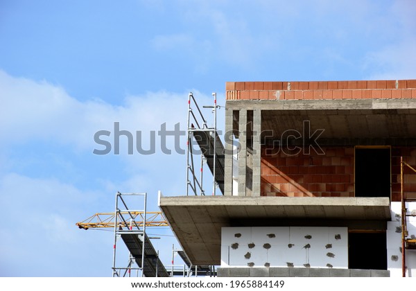 exposed concrete column and slab structure.\
building frame during construction. steel scaffolding. red clay\
block infill. construction concept. cantilevered balcony. styrofoam\
insulation. blue sky