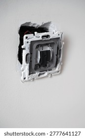Exposed electrical switch box on wall, metal frame with red and black wires visible, rough plaster edges and unpainted cavity, closeup detail for electrician inspection