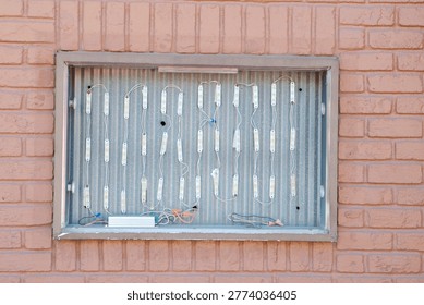 Exposed LED modules and wiring mounted on a corrugated metal panel inside a recessed brick wall box, showing the components of a backlit sign and urban industrial maintenance detail.
