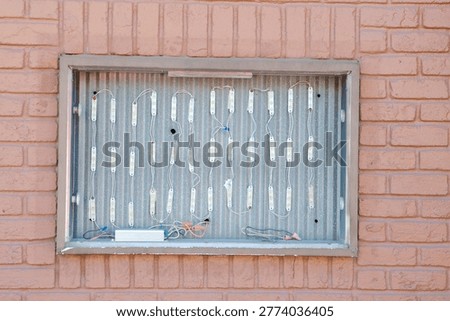 Exposed LED modules and wiring mounted on a corrugated metal panel inside a recessed brick wall box, showing the components of a backlit sign and urban industrial maintenance detail.
