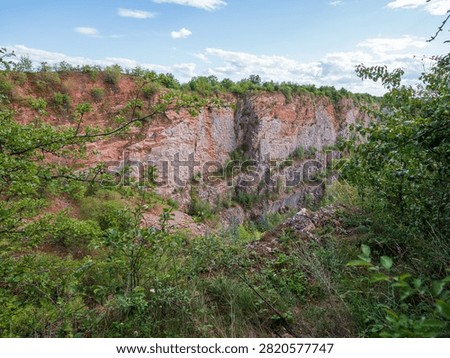 Exposed red Devonian sedimentary rocks and limestone layers at Velka Amerika quarry in the Bohemian Karst, Czech Republic, revealing colorful geological strata.

