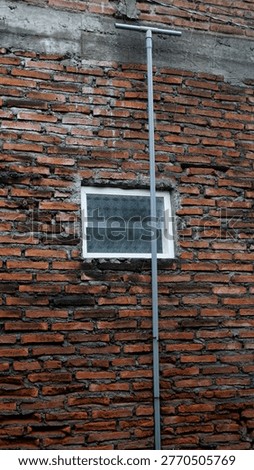 Exposed rough red brick wall with a small glass window and a vertical PVC pipe.