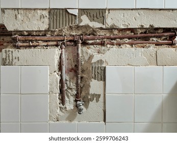 Exposed section of a wall undergoing plumbing work, green pipes are installed within the partially demolished wall, revealing bricks and cemen