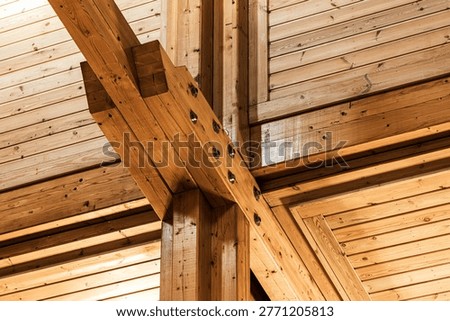 An exposed timber frame ceiling showcasing intersecting heavy wooden beams, visible metal bolts and tongue-and-groove planking, creating a warm, rustic architectural detail