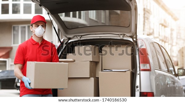 Express
delivery by car and big load of work concept. Courier in protective
mask and gloves get boxes from the car,
outdoor