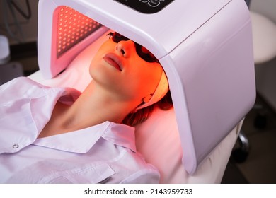 Express facial treatment with led therapy. Beautiful girl on a light therapy procedure. LED lamp with red light. Safe skin care. - Shutterstock ID 2143959733