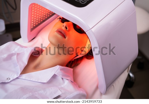 Express facial treatment with led therapy.\
Beautiful girl on a light therapy procedure. LED lamp with red\
light. Safe skin care.