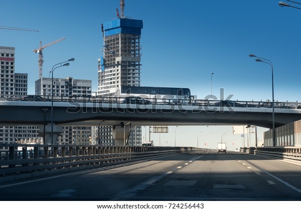 express\
way with white long bus and cars on the background of a huge\
concrete building under construction with\
crane.
