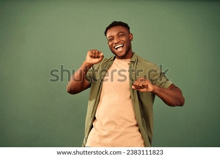 Expressing happiness. Carefree millennial guy wearing unbuttoned khaki shirt joyfully dancing with hands over green background. African american man dynamically moving body while feeling rhythm. [[stock_photo]] © 