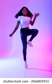 Expressing joy and happiness. Full length portrait of active energetic young black woman jumping in neon light. Excited female model celebrating success or victory, flying in air