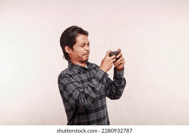 expression of an Asian man in a blue t-shirt and shirt showing excited gestures while standing while playing a game on a cell phone, blurred concept isolated background - Shutterstock ID 2280932787