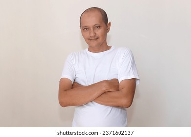 Expression of a bald Asian Indonesian wearing a white t-shirt against a white wall background - Shutterstock ID 2371602137