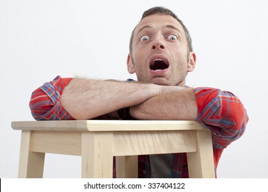 expressive casual man concept - dumbstruck middle age man with checked shirt leaning on wooden stool expressing fear and surprise,white background