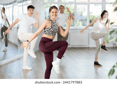 Expressive cheerful young female fitness instructor leading upbeat Zumba class for group in mirrored fitness studio - Powered by Shutterstock