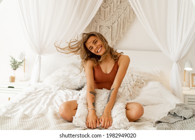 Expressive cute blond woman  sitting in boho bedroom and having fun. Cozy morning home atmosphere. Positive emotions. 