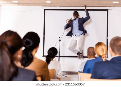 Expressive emotional african american business coach speaking to audience and jumping on stage during motivational training in conference room - Powered by Shutterstock