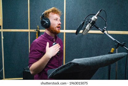 Expressive face of bearded man with red curly hair wear headphones near microphone who makes professional dubbing on a voice recording studio - Shutterstock ID 1963015075