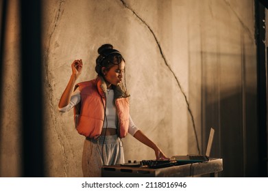 Expressive female DJ in headphones plays music on the remote control and dances on the background of a concrete wall. - Powered by Shutterstock