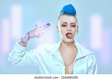 Expressive Girl Punk Rock Musician With Bright Makeup And Blue Mohawk Dressed In Stylish Jacket Putting Fingers To Her Temple And Sticks Tongue Out. Youth Alternative Culture. 