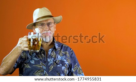 Expressive joyful senior man  in summer hawaiian shirts and straw hat with a mug of beer on a orange studio background. Funny and characteristic.