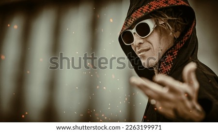 An expressive mature man with dreadlocks, tattoos and sunglasses in black clothes with ethnic ornaments poses on the backstreet. Rock and punk culture. 
